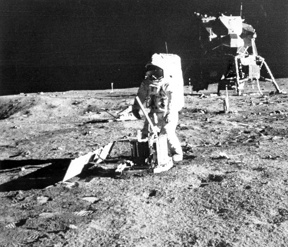 アポロ11号の宇宙飛行士が月面で実験機器を操作している様子。背景には着陸船も写っており、人類初の月面活動をとらえた貴重な記録。