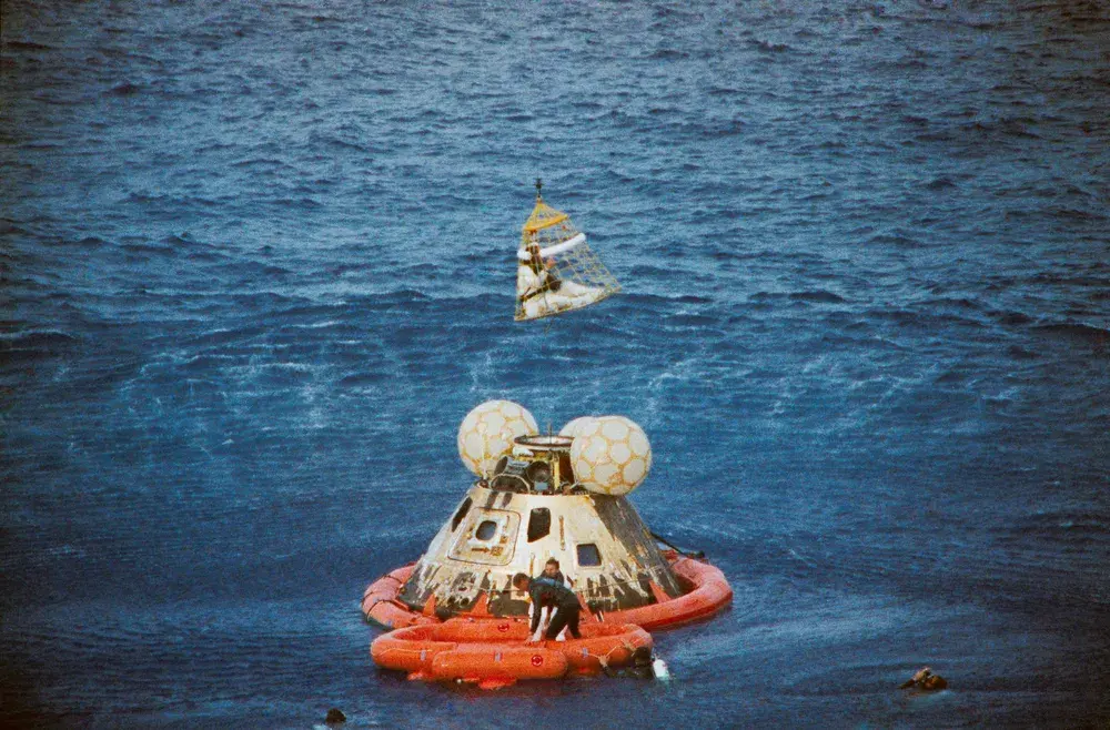 アポロ13号の司令船が地球へ帰還し、海上で宇宙飛行士がヘリに救助されている様子。月面着陸には至らなかったが、奇跡的に生還した歴史的ミッション。